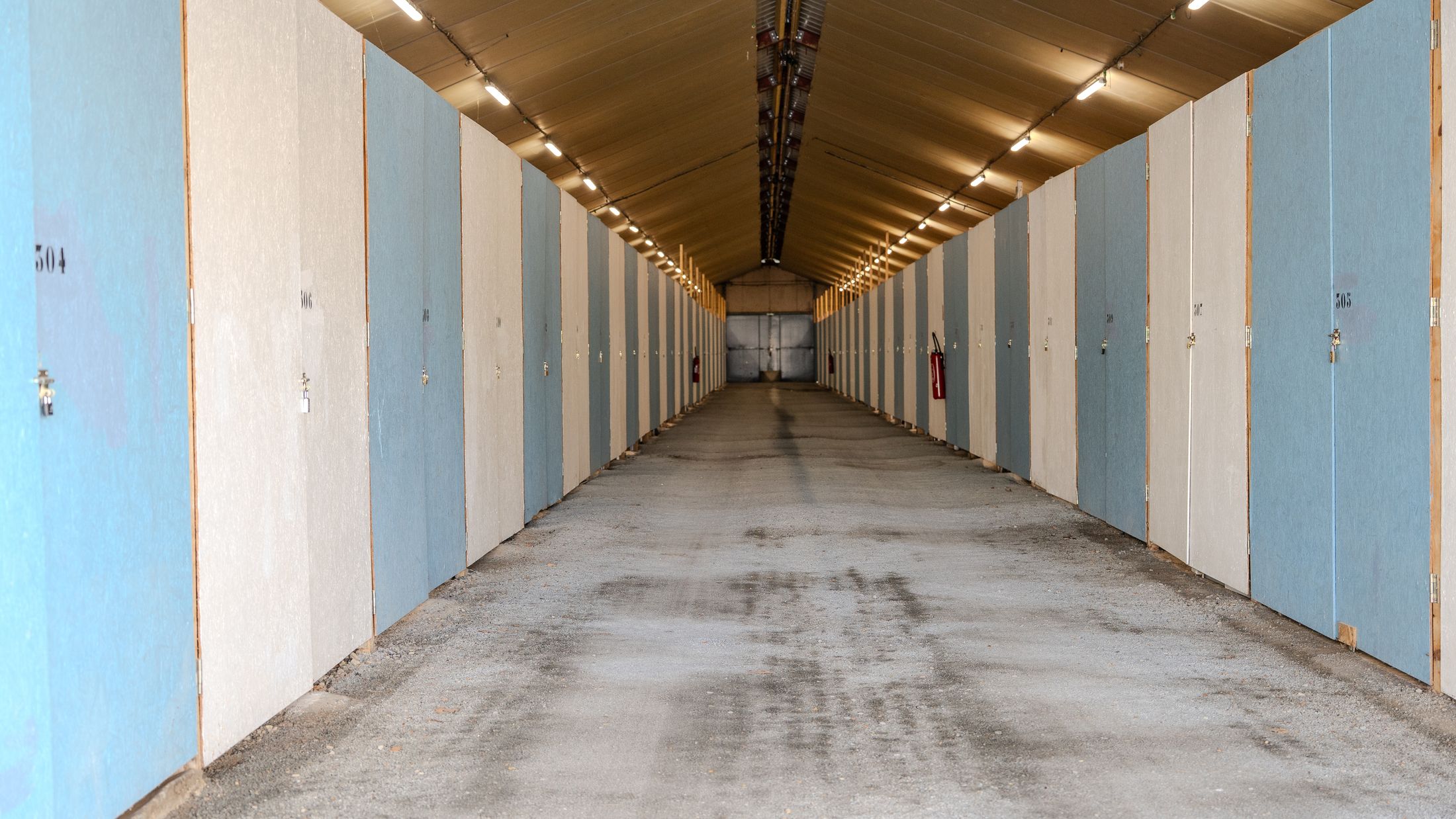Allée intérieure éclairée bordée de box aux portes bleues et blanches