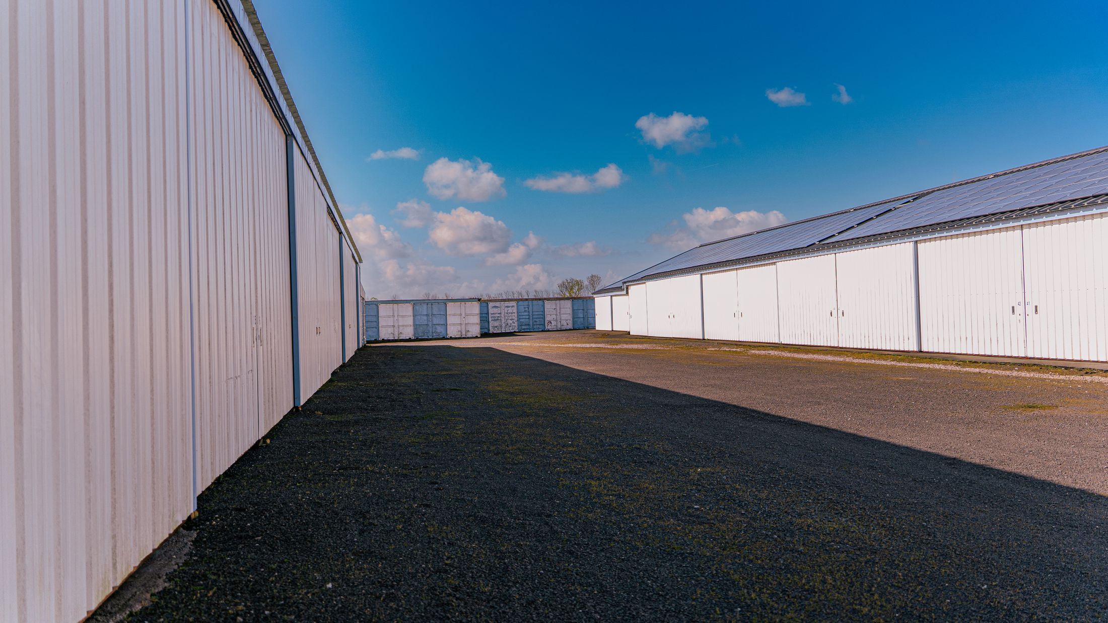 Allée entre deux bâtiments de stockage au bardage blanc, ciel bleu