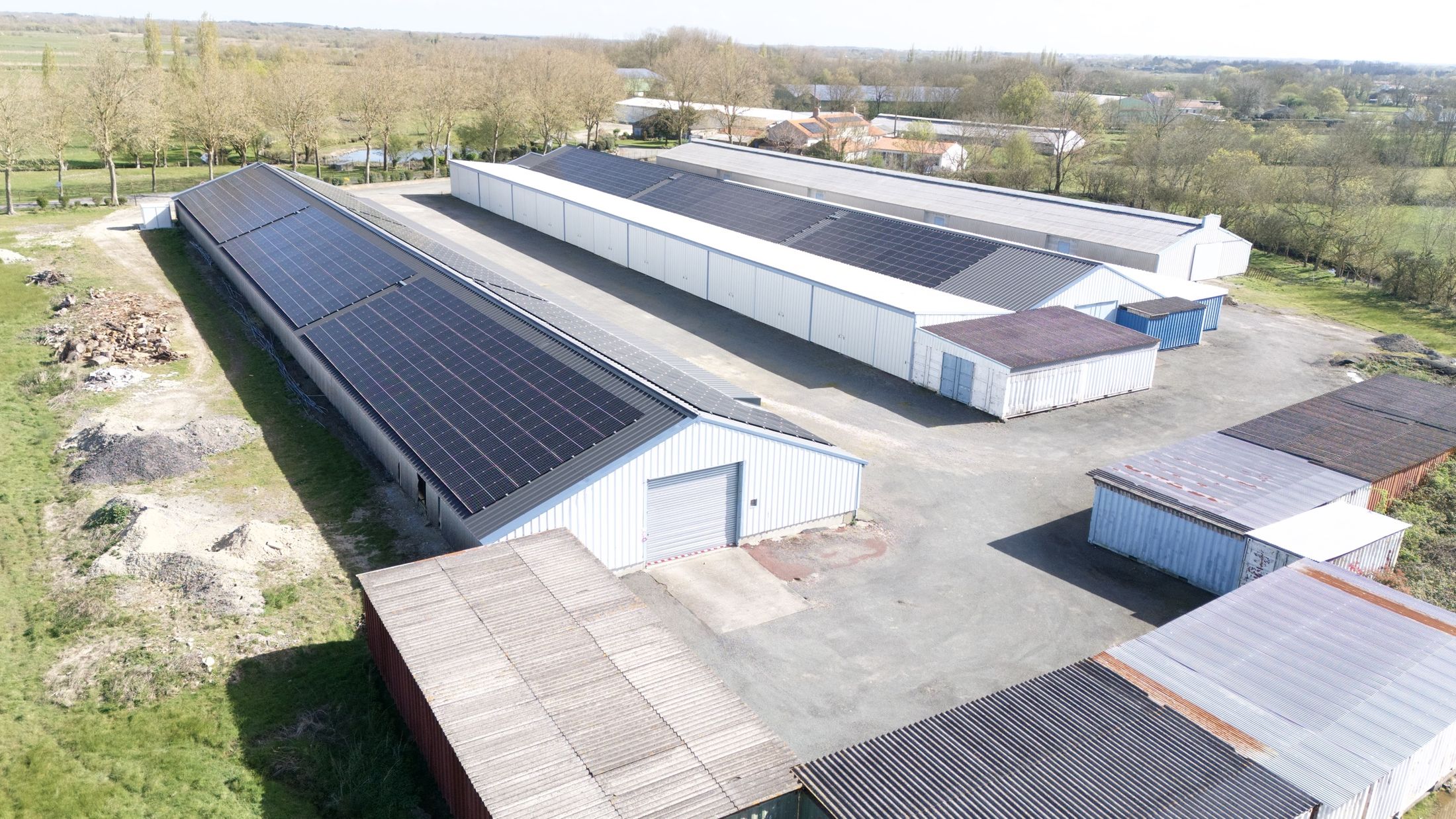 Vue aérienne des bâtiments du Grabat et de leurs toitures solaires, au milieu du bocage